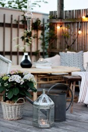 a contemporary deck with rattan furniture, lanterns, watering cans, potted greenery and blooms