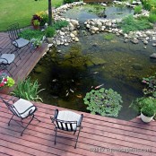 a deck with forged chairs around a large natural-looking pond with fish and pebbles
