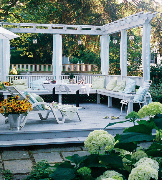 A small and cozy deck in white with a built in bench and several loungers plus potted blooms and greenery