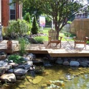 a rustic deck over the pond with rustic wooden furniture and rocks and blooms around