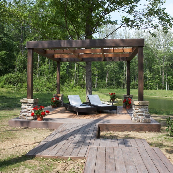 a rustic deck with wicker loungers, potted blooms and a view to the pond