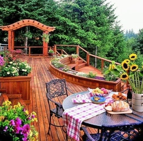 A rustic wooden deck done with warm stained furniture, with forged furniture and potted blooms
