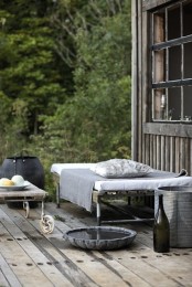 a Nordic deck with weathered wood on the floor and metal furniture – a bed, a chair, table and some buckets