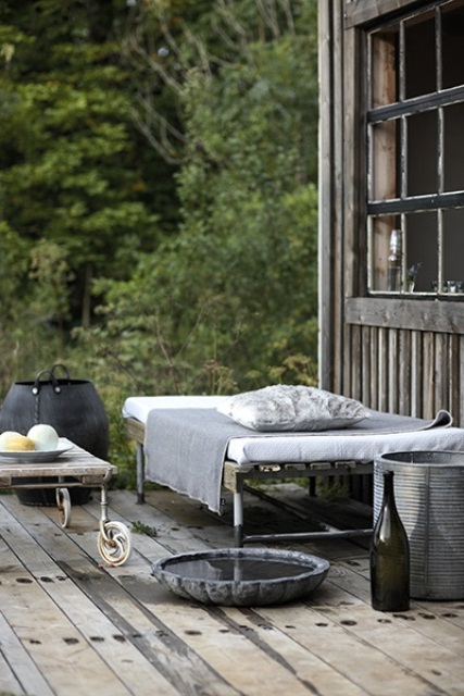 A Nordic deck with weathered wood on the floor and metal furniture   a bed, a chair, table and some buckets