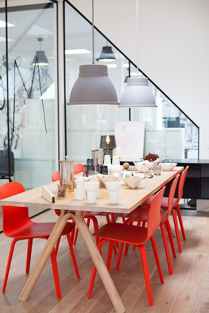 a Scandinavian dining space with a white trestle table, red chairs, grey pendant lamps and white tableware