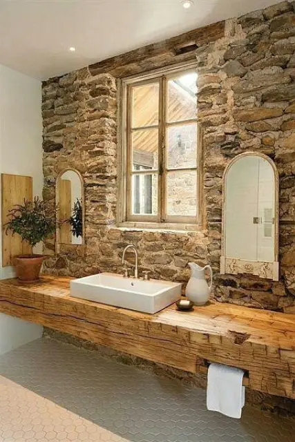a natural stone wall, a wooden vanity and a tile floor for a welcoming light-colored rustic space