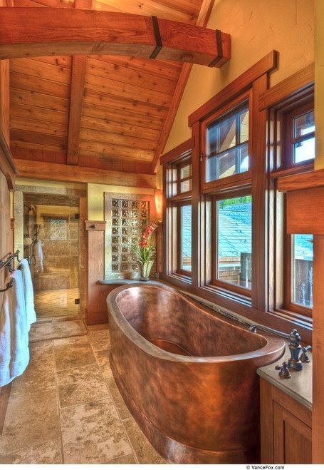 a rustic bathroom with a wooden ceiling and a beam, a wood framed window, a tiled floor and a metal tub