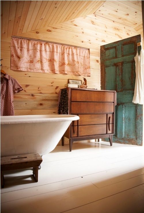 a rustic meets vintage bathroom with a whitewashed wooden floor and light-stained walls plus a sideboard and a door
