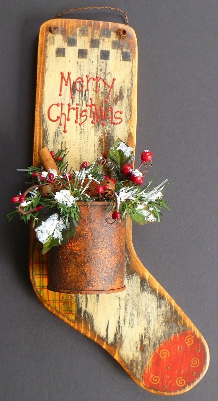 a rustic and shabby chic colorful wooden Christmas stocking with greenery, berries, cinnamon sticks and a metal pot