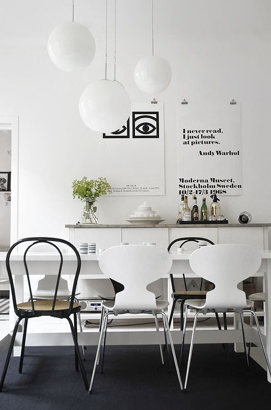 a modern Scandinavian dining room with a white table, mismatching black and white chairs, a sleek white credenza with a wooden countertop and a black and white gallery wall