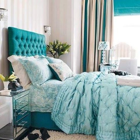a neutral bedroom with a turquoise upholstered bed with an extended headboard, aqua blue bedding, turquoise and tan curtains looks chic, bold and very lively