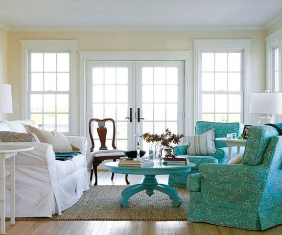A neutral living room with a vintage touch, light yellow walls, a white sofa, turquoise chairs and a coffee table and a vintage dark stained chair