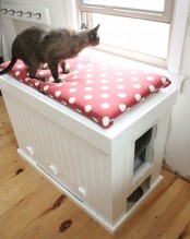 a white storage cabinet with a polka dot cushion on top and a cat litter box inside