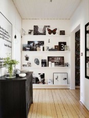 a blank white wall turned into a gorgeous gallery wall with white ledges and lots of black and white artworks and greenery