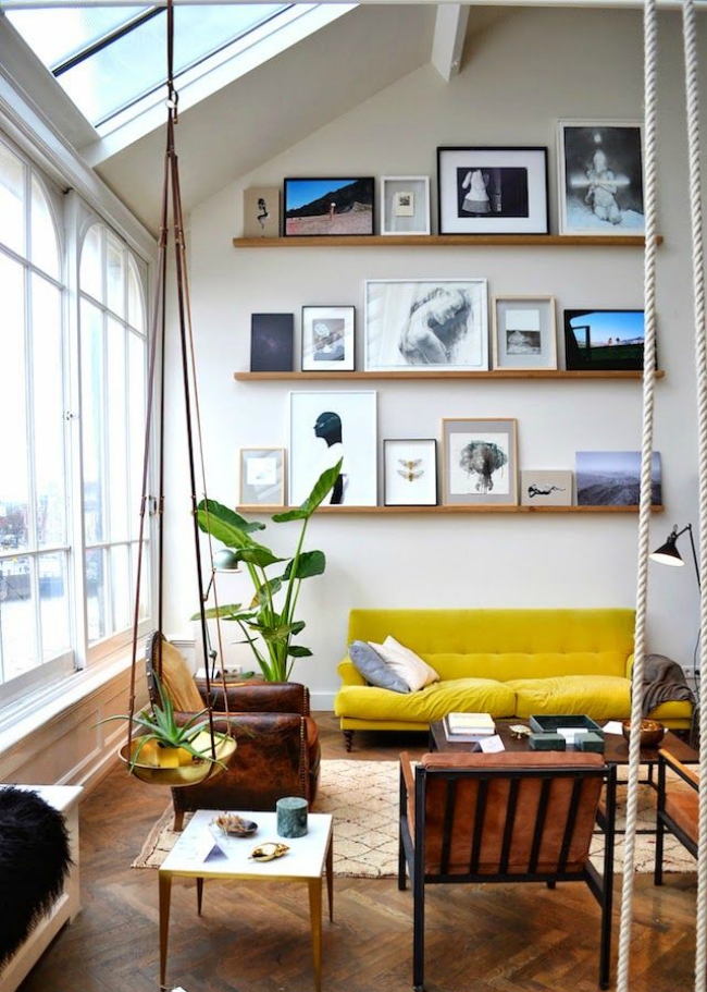 A bold double height living room with lots of natural light, bold furniture, ledges with cool and bold artworks plus potted plants and greenery