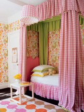 a dreamy country girl’s room with bright floral wallpaper, a canopy bed in pink and neutrals, gingham curtains and a bold printed rug