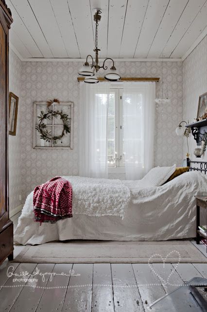 fur and plaid blankets and a greenery wreath make this all-white bedroom very welcoming and very winter-like