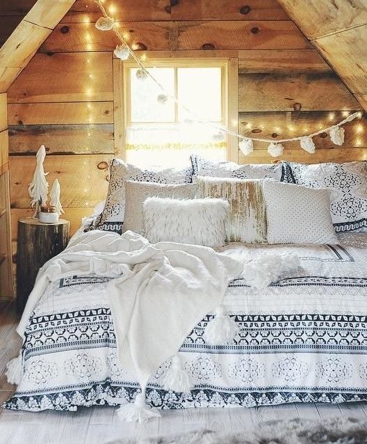 a cozy cabin winter bedroom all clad with rough wood, with lights, a pompom garland and lots of fluffy pillows