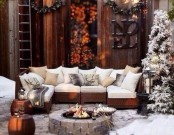 a stylish winter terrace with a large white sofa, lots of pillows, a large fire pit, a couple of snowy Christmas trees and woven side tables