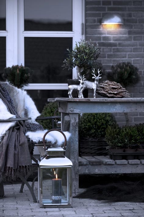 moody winter terrace decor with a shabby rustic table, potted greenery, deer, a wooden chair with faux fur and a large lantern
