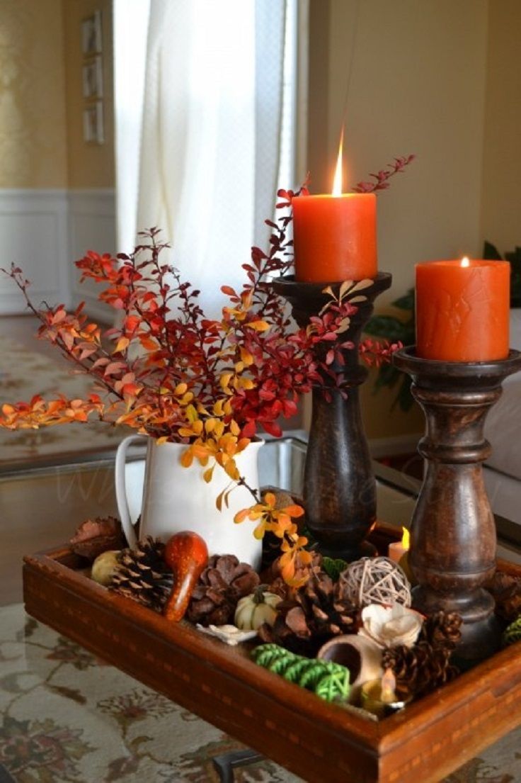 A fall centerpiece of a tray with pinecones, pumpkins, gourds and fall leaf branches plus rust colored candles for a bright touch