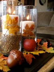 a fall centerpiece of acorns, fall leaves and pillar candles in glasses with corn and fall leaves is lovely and easy to DIY