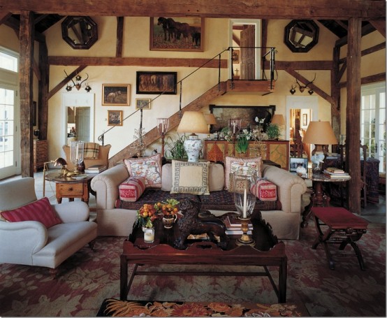 a barn living room with wooden beams and pillars, with a vintage gallery wall, neutral seating furniture, stained stools and tables and chic lamps