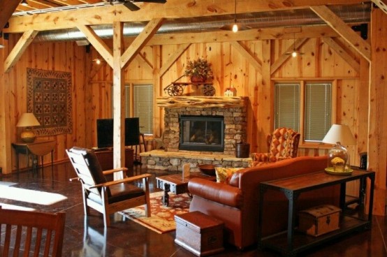 a wood clad barn living room with a fireplace clad with stone, leather and wood furniture, lamps and hanging bulbs is cozy