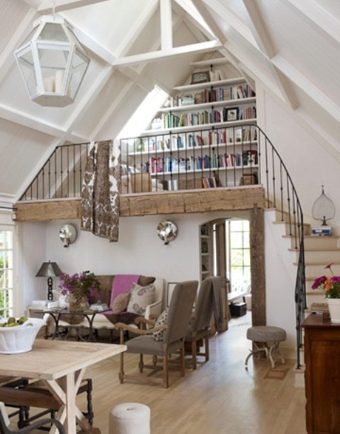 A neutral barn living room with a wooden beam and pillar, with neutral seating furniture, a trestle dining table and a reading nook with lots of built in bookshelves