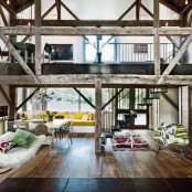 a barn living room with lots of pillars and beams of reclaimed wood, with neutral and colorful furniture, colorful and printed textiles is a cool idea