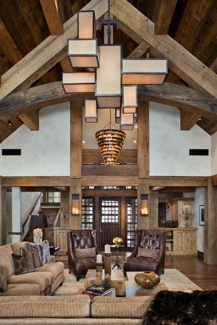 A barn living room with wooden beams and pillars, with neutral seating furniture, brown leather chairs, a stone coffee table and a very eye catchy cube chandelier