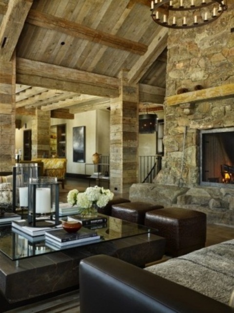 a barn living room with reclaimed wood walls and a ceiling, a fireplace clad with stone, dark leather furniture and a glass and stone coffee table is amazing