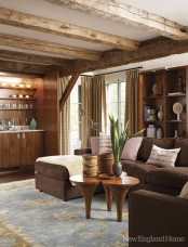 a barn living room with wooden beams, a built-in wooden bar, a brown sectional, a creative coffee table and built-in wooden shelves