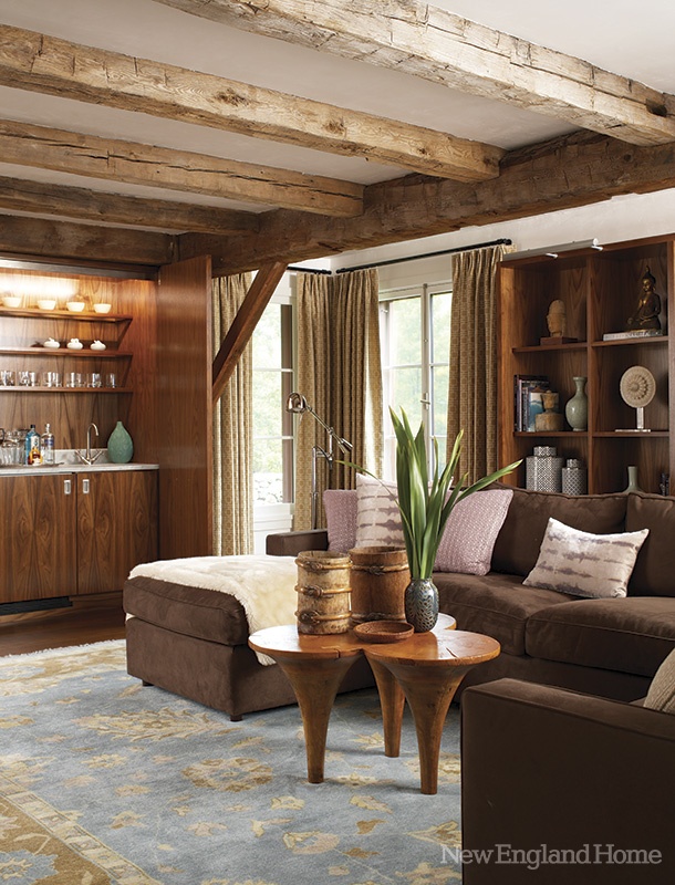 A barn living room with wooden beams, a built in wooden bar, a brown sectional, a creative coffee table and built in wooden shelves