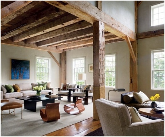 A barn living room with wooden beams and pillars, with chic contemporary furniture, neutral and dark, with low coffee tables and a bold artwork is amazing