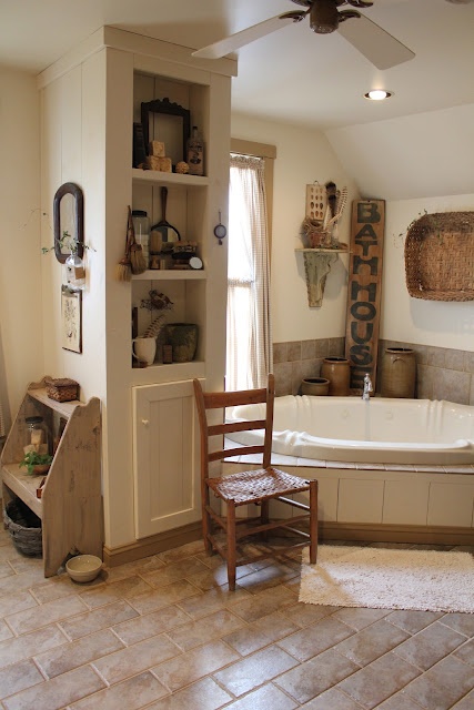 a cozy neutral farmhouse bathroom with earthy tiles on the floor and walls, a storage unit and a sunken bathtub