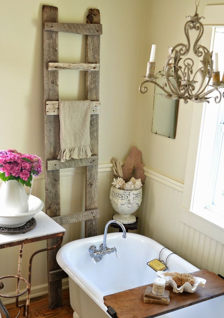 A neutral warm colored farmhouse bathroom with sandy walls, white beadboard, a clawfoot bathtub and an old ladder to hang towels