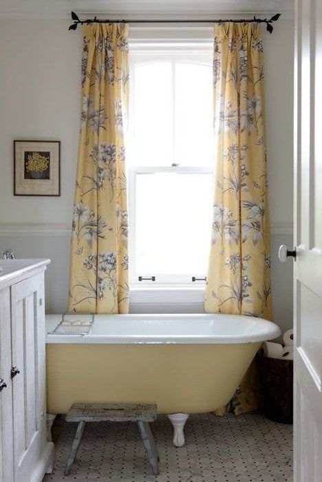 a small farmhouse bathroom with a white vanity, a yellow clawfoot bathtub, yellow printed curtains