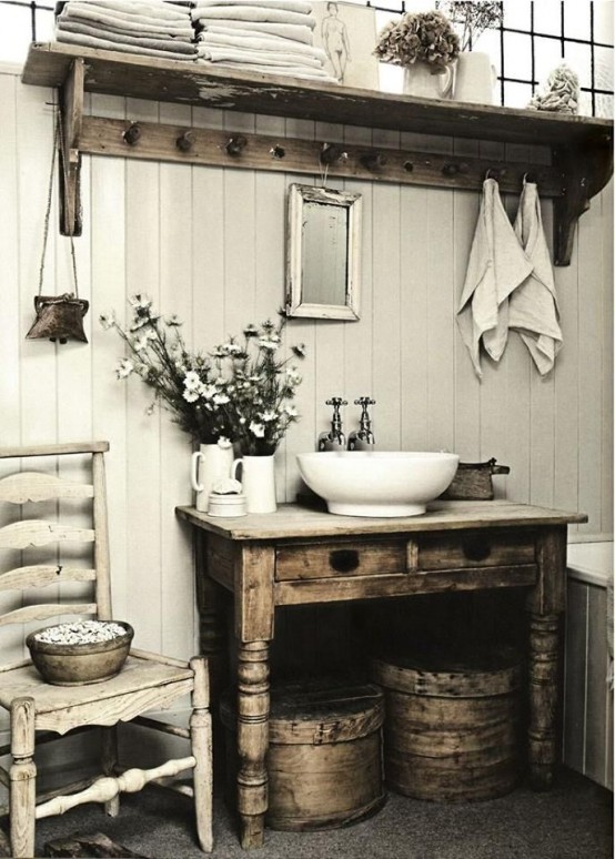 a shabby chic farmhouse bathroom with white plank walls, shabby wooden furniture, a vintage chair and round wooden boxes for storage