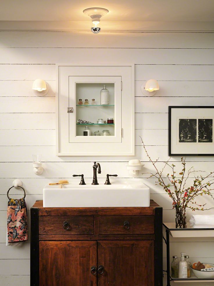 A white farmhouse bathroom with planks on the walls, a rich stained wooden vanity and a built in apothecary storage unit