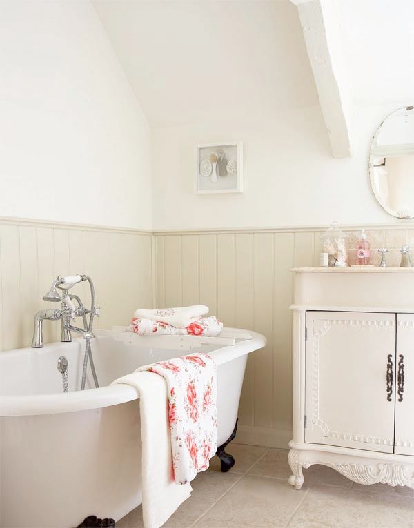 A cute and welcoming farmhouse bathroom in creamy and off white, a blush bethtub, off white beadboard and a vintage vanity