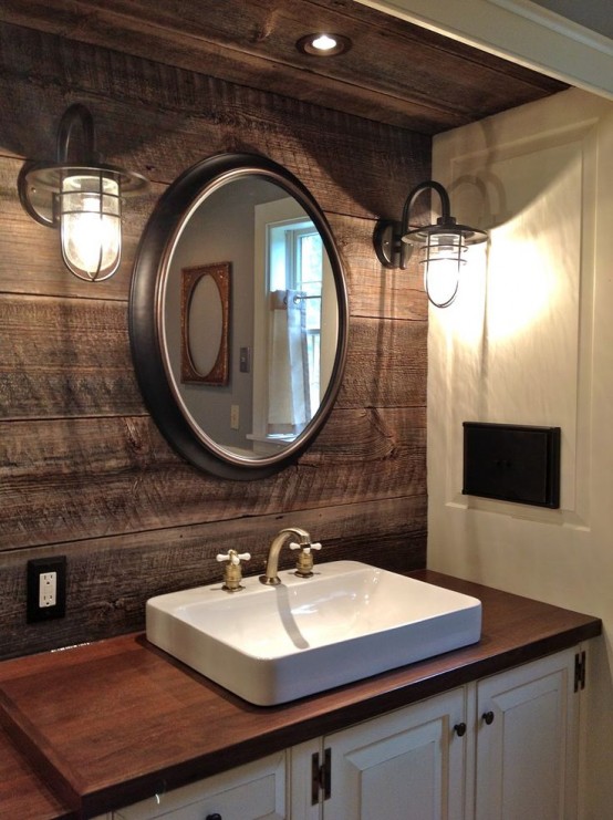 a rustic bathroom with a weathered wooden wall, wall lamps, a white vanity with a wooden top and a square sink