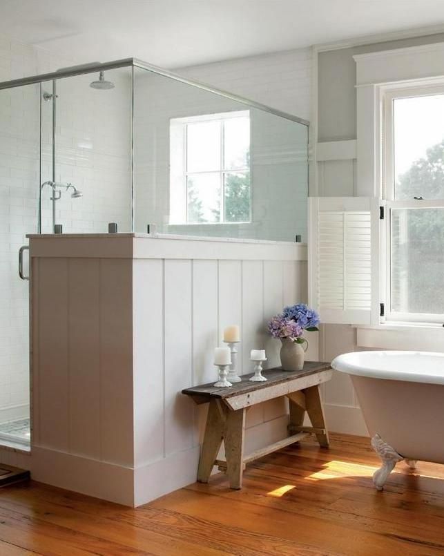 A cozy and light filled neutral farmhouse bathroom with a clawfoot bathtub, a shower partly clad with beadboard