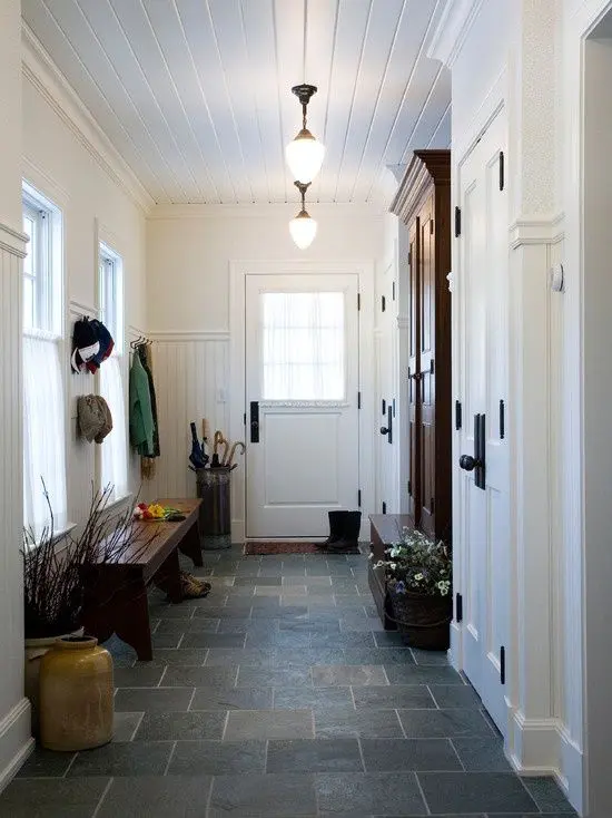 a farmhouse mudroom done in white with a grey tile floor, dark furniture and soem branch arrangements