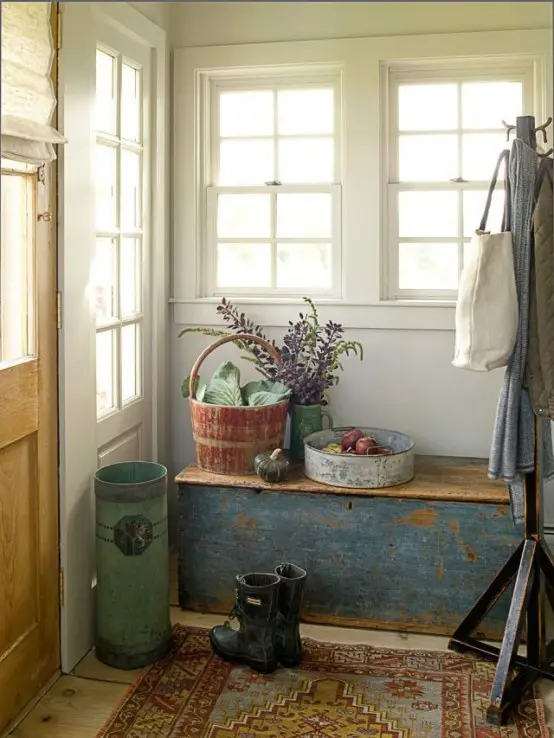 a rustic meets shabby chic entryway with a shabby blue chest, a rug and some wooden baskets for storage
