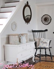 a white vintage sideboard, a black vintage chair, a round mirror and tin cans for storage plus a FARM pillow