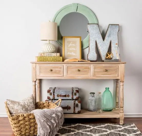 a cozy vintage meets rustic entryway with a woodne console, some metal suitcases, a metal monogram and a basket for storage
