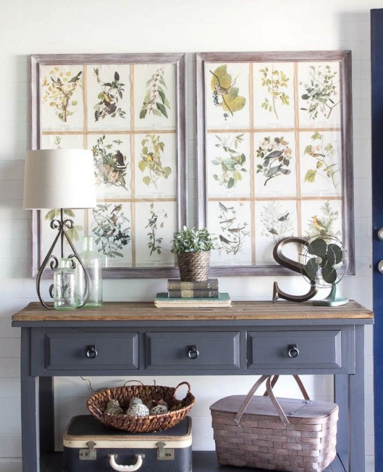 a grey console table with a stained tabletop, vintage posters as artworks, baskets and a potted plant for a cozy farmhouse entryway
