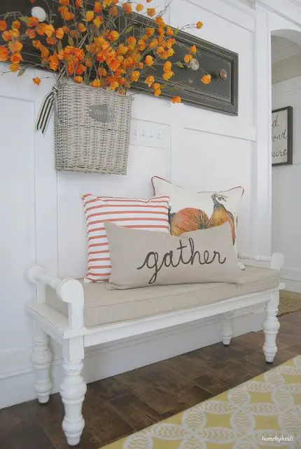 a small fall farmhouse entryway with a vintage white bench, bright pillows, a bold arrangement hanging on the rack