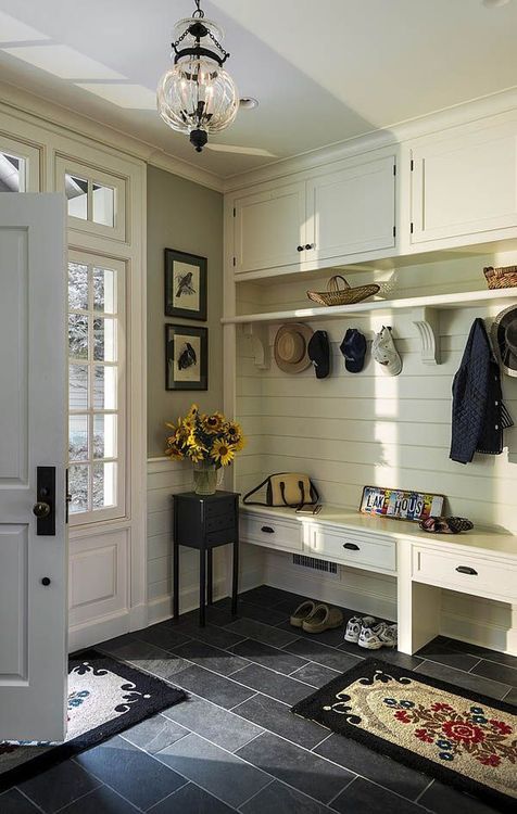 A farmhouse entryway with an ivory wooden furniture piece iwth a built in bench of drawers and more storage space plus dark tiles on the floor for a contrast